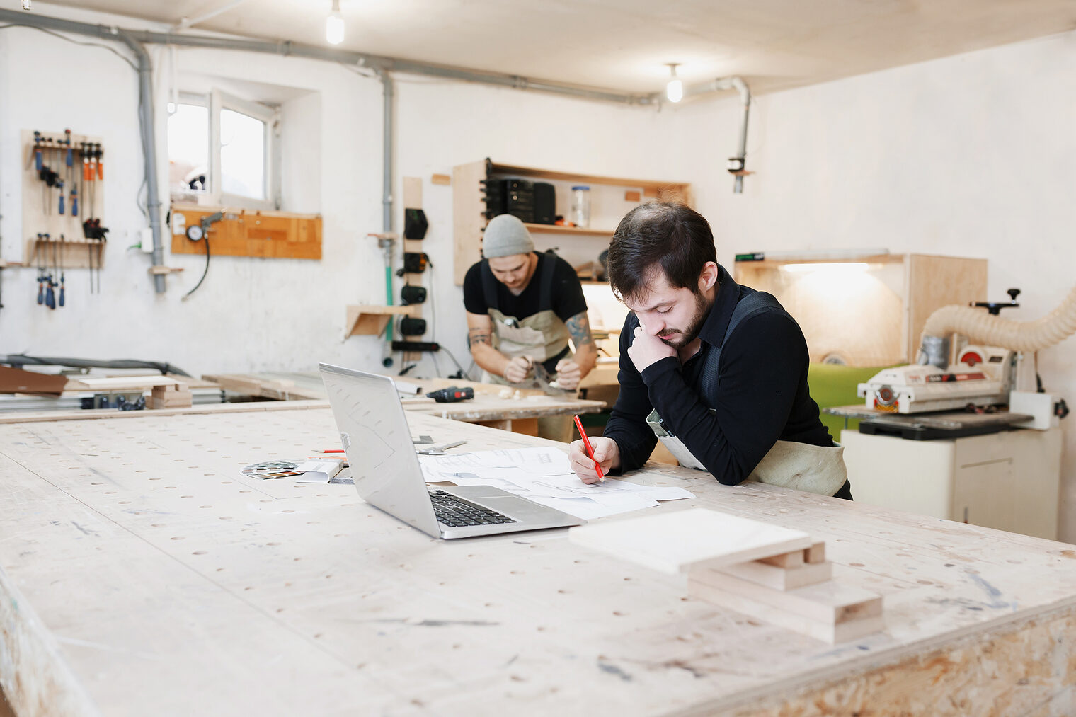 Portrait of a carpenter standing in his woodwork studio and works on the project. Startup business, young specialist, carpenter's profession. use of the laptop Schlagwort(e): people, workshop, woodshop, woodwork, work, workbench, carpenter, job, business, carpentry, profession, professional, adult, bench, caucasian, craft, craftsman, expertise, male, man, manual, occupation, person, skill, studio, tool, wooden, worker, young, app, authentic, beard, rugged, shelf, maintenance, design, standing, board, wifi, texture, real, repair, manufacturing, plans, workman, technology, protection, digital, build, laptop